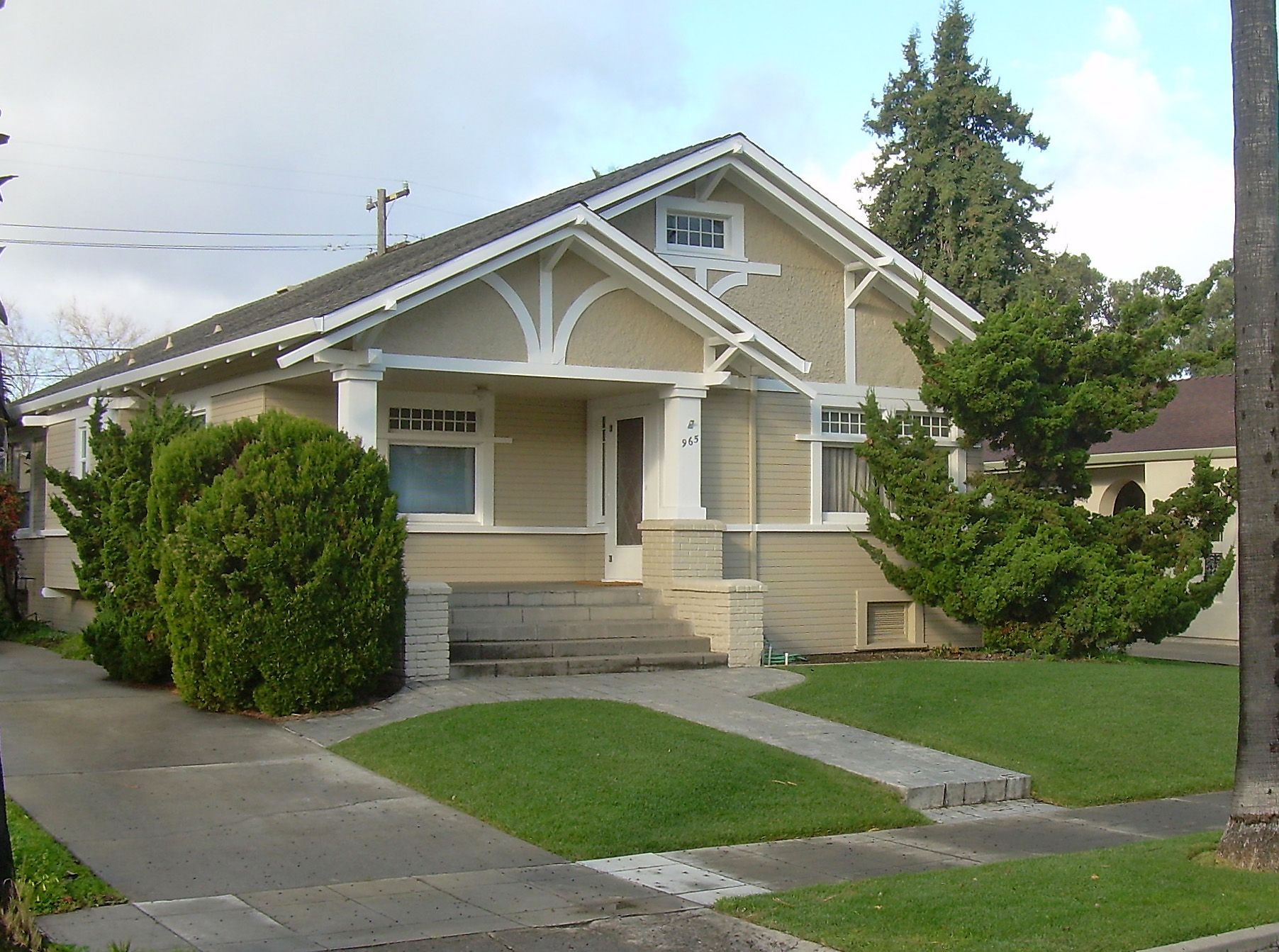 A single-story craftsman bungalow in San Jose with wood siding and a gabled porch, raised above the lawn on a low foundation wall, with a louvered vent set into the foundation below the siding and clipped shrubs growing against the wall.